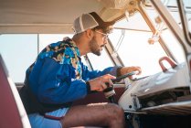 Side view of handsome young man in stylish outfit sitting on driver seat and steering retro van while travelling — Stock Photo