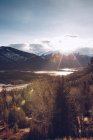 Яскраве сонце, що сяє на небі з невеликою кількістю хмар над атлантичним канадським лісом на задньому плані з сніжними горами та маленьким озером. — стокове фото