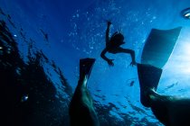 Criança irreconhecível nadando em direção às pernas em nadadeiras enquanto snorkeling na água do mar azul — Fotografia de Stock