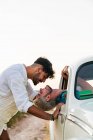 Вид збоку на чоловіка, що сидить всередині машини і виходить з вікна, цілується з хлопцем, що стоїть надворі влітку — стокове фото