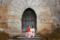 Attractive Multiethnic ladies sitting on steps near tower's door and looking away — Stock Photo