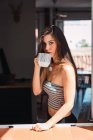 Porträt einer jungen Frau, die am Fenster Kaffee trinkt — Stockfoto