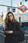 Mujer sosteniendo teléfono inteligente cerca de metro en la ciudad - foto de stock