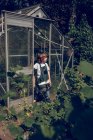Boy standing in font of greenhouse and looking away — Stock Photo