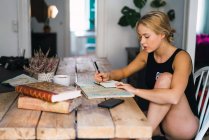 Femme blonde assise à table avec des livres, carte et café et voyage de planification — Photo de stock