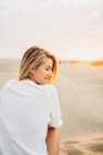 Молода усміхнена жінка в білій футболці сидить на піску на заході сонця — стокове фото