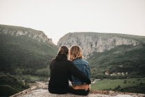 Bonito casal abraçando enquanto sentado em encosta rochosa no fundo do belo vale e montanhas — Fotografia de Stock