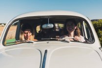 Group of happy multiethnic women in car driving together in bright sunlight and laughing — Stock Photo