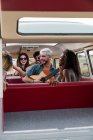 Gruppe junger Leute lacht und hört dem gutaussehenden Mann zu, der in einem Oldtimer-Van in der Natur Akustikgitarre spielt — Stockfoto