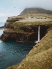 Grüne felsige Klippen und sprühender Wasserfall auf Feroe Islands — Stockfoto