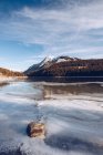 Річка, що біжить у таненому високогірному озері на засніженому щілині з коричневими скелями та кількома зимовими ярмарками у сонячний день — стокове фото