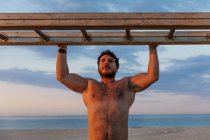 Бородатий без сорочки чоловік піднімається по дерев'яній драбині під час тренувань на пляжі — стокове фото