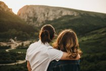 Linda pareja abrazándose mientras está sentado en la ladera rocosa en el fondo del hermoso valle y las montañas - foto de stock