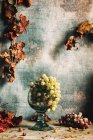 Raisins verts dans une tasse en verre sur une surface en bois avec des raisins violets et des feuilles d'automne sèches — Photo de stock