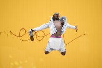 Homem americano africano pulando com dispositivo de rádio vintage no fundo amarelo — Fotografia de Stock