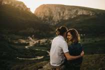 Coppia carina abbracciare e dure fronti mentre seduto sul pendio roccioso sullo sfondo di bella valle e montagne — Foto stock