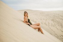 Porträt einer sinnlichen jungen Frau im schwarzen Badeanzug, die auf einer Sanddüne liegt — Stockfoto