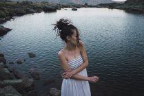 Mujer joven en vestido de pie cerca del lago ondulante - foto de stock