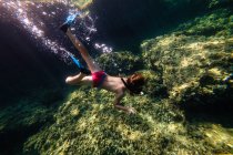 Menino irreconhecível mergulho no mar perto da rocha — Fotografia de Stock