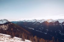 Winter forest on snowy hills on background with cloudy sky and sunshine?with picturesque mountains with highland rivers — Stock Photo