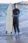 Porträt eines gutaussehenden Mannes mit seinem Surfbrett am Strand — Stockfoto