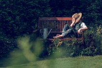 Garçon en chapeau de paille reposant sur le banc dans le jardin — Photo de stock