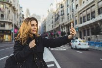 Woman taking selfie with smartphone on road in city — Stock Photo