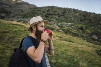 Молодий чоловік в капелюсі стоїть в горах з чашкою — стокове фото