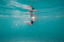 Menino em calções de banho nadando na piscina profunda turquesa transparente — Fotografia de Stock