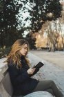 Junge Frau sitzt auf Parkbank und liest Buch — Stockfoto