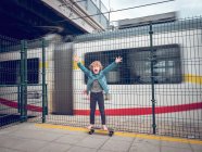 Lustiger barfüßiger Junge auf Skateboard mit erhobenen Händen vor Zug — Stockfoto