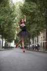 Bailarina de cabeza roja con tutú negro y consejos de ballet rojo bailando en la calle con árboles en el fondo . - foto de stock