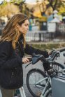 Молода жінка бере велосипед з парковки в міському парку — стокове фото