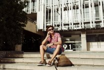 Молодий турист розмовляє по смартфону і сидить на сходах у місті — стокове фото