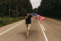 Человек с флагом США бежит по дороге — стоковое фото
