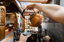Crop mão derramando água de bule de cobre para copo durante a cerimônia do chá oriental — Fotografia de Stock