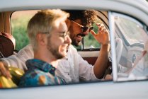 Two young guys laughing and holding map while sitting inside retro car during nice travel — Stock Photo