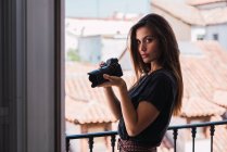 Young woman standing at balcony with photo camera in old city — Stock Photo