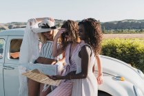 Donne multietniche alla moda in piedi vicino auto d'epoca e mappa di lettura mentre viaggiano insieme in estate — Foto stock