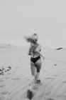Anonymous blonde woman in swimwear running on sand — Stock Photo