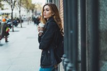 Mujer joven con taza de papel de café de pie en la calle - foto de stock