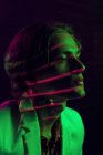 Attraente uomo androgino tenere gli occhi chiusi mentre in piedi sotto illuminazione colorata in camera oscura — Foto stock