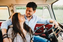 Cheerful young man and woman embracing and riding in vintage van on road in rural environment — Stock Photo