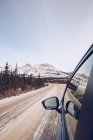 Clean pickup with people driving on Canadian forest road with many firs and on background with snowy mountains and cloudy sky — Stock Photo