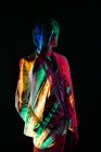 Андрогінна чоловіча модель в костюмі, що стоїть в розслабленому положенні під барвистим освітленням на чорному тлі — стокове фото