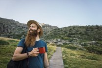 Jovem de pé no caminho nas montanhas com copo e olhando para longe — Fotografia de Stock