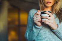 Крупным планом женщины в сером свитере, держащей чашку с напитком — стоковое фото