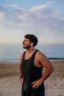 Fiducioso uomo barbuto in piedi sulla spiaggia al tramonto — Foto stock