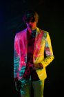 Androgynes männliches Modell im Anzug steht in entspannter Pose unter farbenfroher Beleuchtung auf schwarzem Hintergrund — Stockfoto