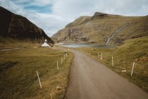 Perspectiva de un pequeño camino hacia el lago entre acantilados en las Islas Feroe - foto de stock